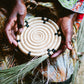 Hand holding a woven basket with decorative elements on a patterned fabric background