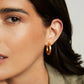 Close-up of a woman wearing gold hoop earrings with a neutral background