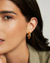 Close-up of a woman wearing gold hoop earrings with a neutral background