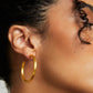 Close-up of a person wearing a gold hoop earring with a neutral background