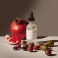 Bottle of face oil with a pomegranate and olives on a neutral background
