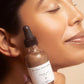 Person holding a bottle of 'Beauty from the Root' face oil near their face.