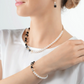 View of a blonde model in a white shirt wearing the GeoCUBE onyx and gold pearl fusion collection featuring a bracelet, necklace and earrings.