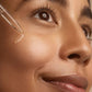 Close-up of a woman applying skincare product with a dropper on her face.
