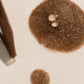 Brown makeup product with applicator on a beige background