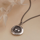 Silver necklace with a round pendant on a beige surface with dried leaves.