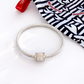Silver bracelet with a decorative clasp on a white surface with a patterned bag in the background.