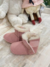 Angled view of a pair of pink suede baby booties with a white lining and a velcro strap
