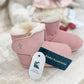 Angled view of a pair of pink suede baby booties with a white lining and a velcro strap