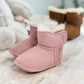 Angled view of a pair of pink suede baby booties with a white lining and a velcro strap