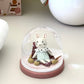 Small figurine inside a glass dome on a white surface with decorative elements.