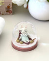 Small figurine inside a glass dome on a white surface with decorative elements.