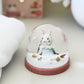 Decorative snow globe with a figurine of a rabbit in a snowy scene, placed on a light surface.