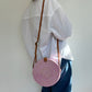 Person wearing a white shirt and blue jeans with a pink woven handbag on a plain background