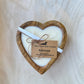 Heart-shaped candle in a wooden holder with a tag on a light wooden background
