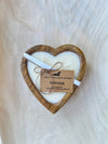 Heart-shaped candle in a wooden holder with a tag on a light wooden background
