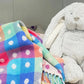 A multicolored geometric patterned baby blanket with polka dots, draped over a surface with a large plush toy beside it.