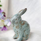 Ceramic rabbit figurine with a distressed finish on a white surface with flowers in the background
