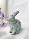 Ceramic rabbit figurine with a distressed finish on a white surface with flowers in the background