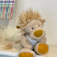 Plush lion toy on a shelf with a colorful plaid blanket in the background