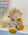 Plush lion toy on a shelf with a colorful plaid blanket in the background