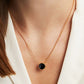 Necklace with a black pendant worn by a person in a white outfit