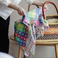 Person holding a colourful polka dot blanket over a woven moses basket