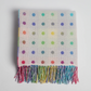 Multicolored polka dot blanket with fringes on a light gray background