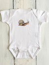 White baby onesie with a snail design on a wooden surface