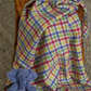 Colourful tartan blanket draped over a chair with a blue teddy bear on a carpeted floor.