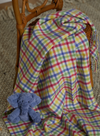 Colourful tartan blanket draped over a chair with a blue teddy bear on a carpeted floor.