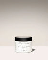 Jar of baby body balm with a black lid on a light beige background