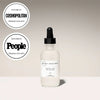 White face oil bottle with black dropper on a beige background, featuring 'Cosmopolitan' and 'People' logos.